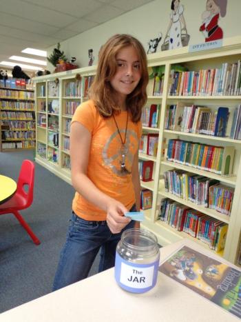 Taylor Robertson, the first participant to complete the Summer Reading Program at the Wiscasset Public Library, deposits her name into the jar. Because she also read a biography, she will place her name in the jar a second time. Three participants who complete the reading requirements of the program have an opportunity to be awarded a Kindle if their names are drawn from the jar. Taylor is the daughter of Tracy Robertson. Courtesy of Wiscasset Public Library