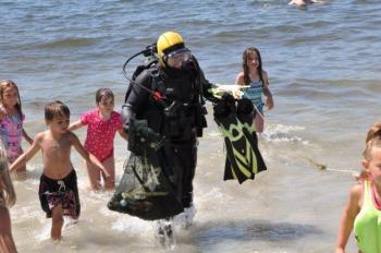 Young beach-goers swarm around Brian Boone as he returns with a bag full of sea creatures and other found items. From a 45-minute dive, Boone culled squid eggs, a juvenile lobster, several hermit crabs, a golf ball, a quahog and one feisty rock crab from the waters off Pemaquid Beach. BEN BULKELEY/Boothbay Register