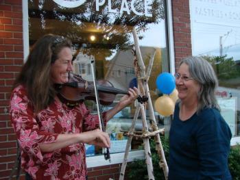 Liz Lannon, left, of Wiscasset on fiddle meets up with twig artist Susan Perrine of Woolwich outside Mac's Place during the art walk. SUSAN JOHNS/Wiscasset Newspaper