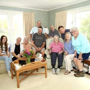 Evelyn Luther Pratt Sherman holds the Boston Post Cane surrounded by her family — Kali Andrews, Cory Chase, Anne Thompson Maher (cousin), Jack Sherman (grandson), Jerry McGrail (son-in-law), Mary Lou Thompson Koskela (cousin), Jake Brewer (grandson), Sarah Sherman (daughter), and Susan Jellison (daughter). Robert Mitchell photo